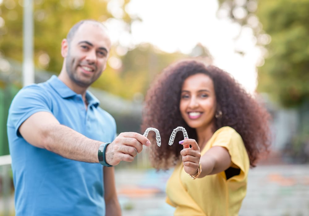 Smiling couple proudly showing their clear aligners, highlighting a modern approach to achieving perfect smiles together - Invisalign