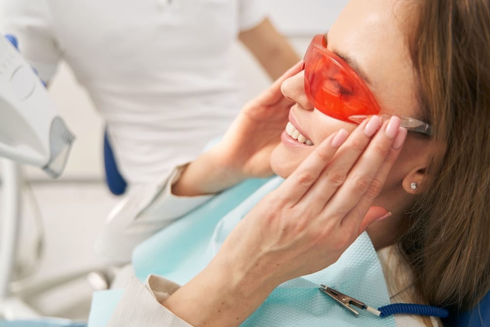Woman Wearing Protective Glasses for Laser Teeth Whitening - Laser Dentistry Smiling woman wearing safety glasses during a professional laser teeth whitening treatment for a brighter smile - Laser Dentistry