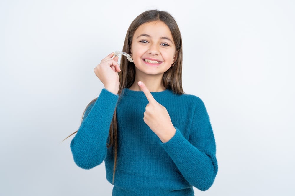 Young girl pointing to her clear aligner, showcasing a kid-friendly, comfortable solution for straightening teeth. - Invisalign