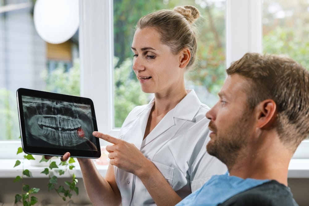 Dental professional pointing to a digital X-ray on a tablet, explaining findings and recommended dental care.