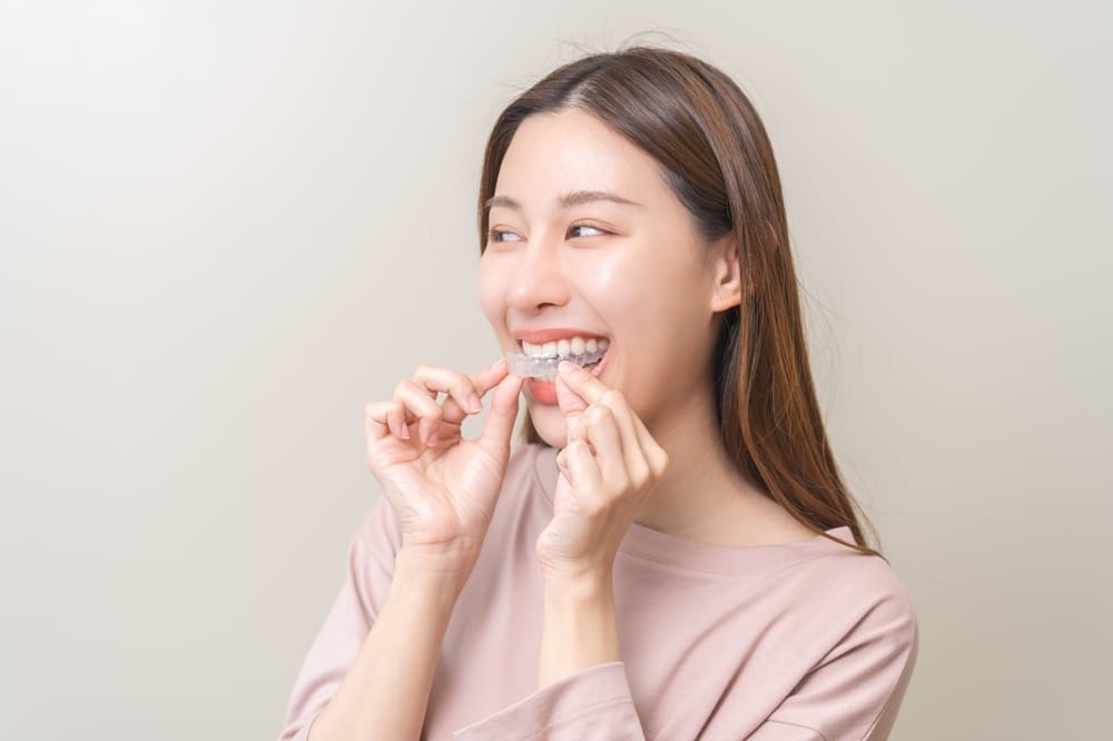 Young woman placing a clear aligner over her teeth, enjoying an invisible and convenient orthodontic solution. - Invisalign