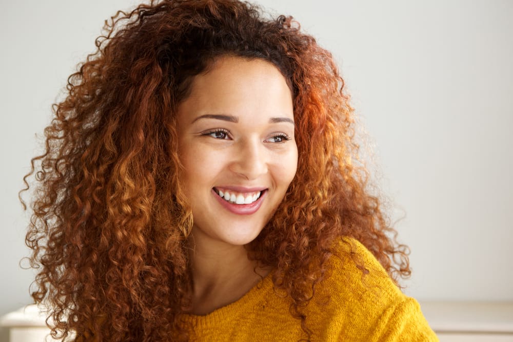 Attractive woman with curly hair smiling warmly, highlighting her bright, well-maintained teeth. - Teeth Whitening